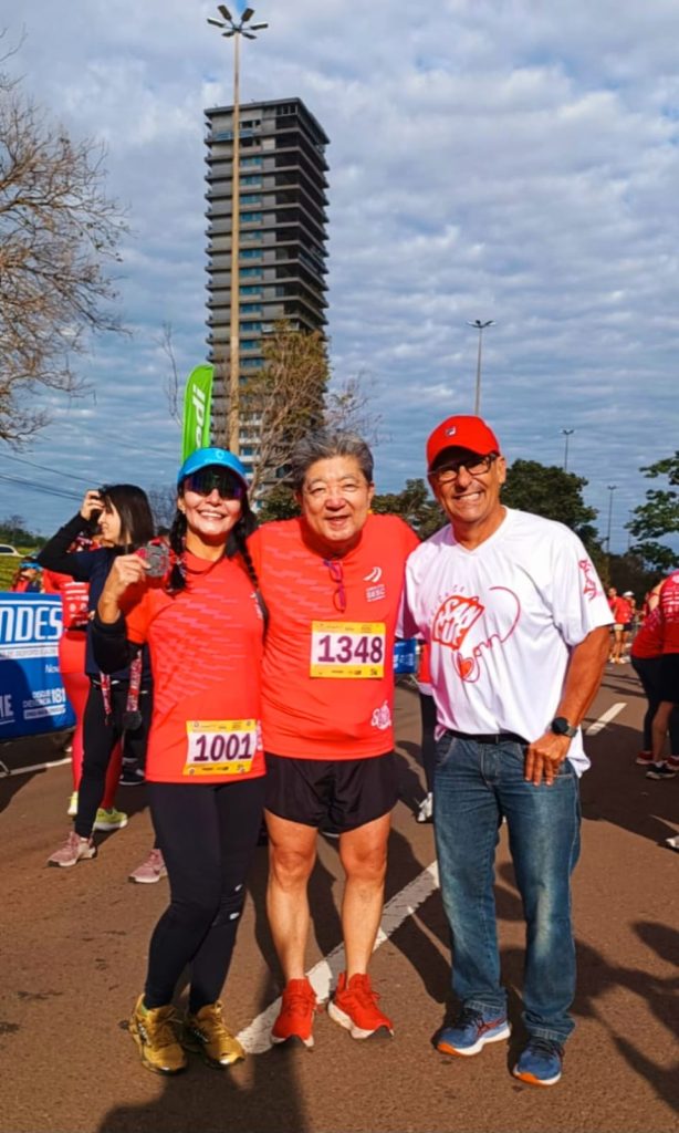 Foto com tres pessoas em destaque, duas com roupas de corrida.