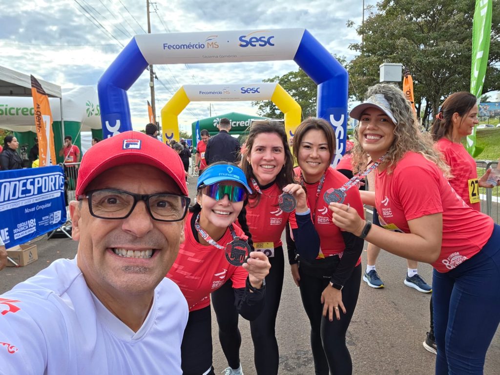 Foto de possoas sorridentes sendo um home e quatro mulheres, tres delas estão mostrando a medalha.